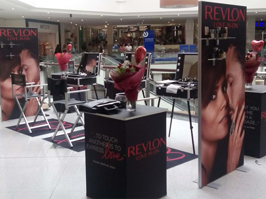 Revlon vertical banners and branded plinths with black backgrounds and red lettering at a shopping centre activation