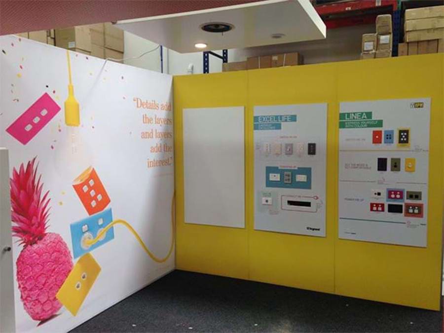 Stand mock-up with a full-height printed graphic on one wall and printed product panels on yellow walls beside it