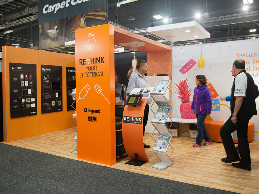 Legrand and HPM exhibition stand in orange with a light wood-grain floor finish and brochure stands