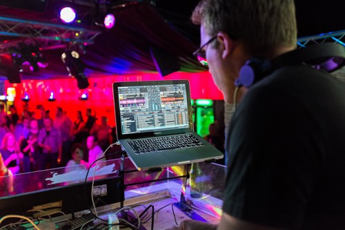DJ mixing music on a laptop for a crowd in a nightclub
