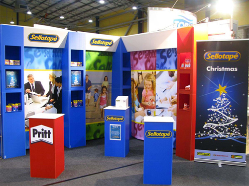 Sellotape and Pritt exhibition stand with blue shelving walls, branded plinths and a Christmas pull-up banner