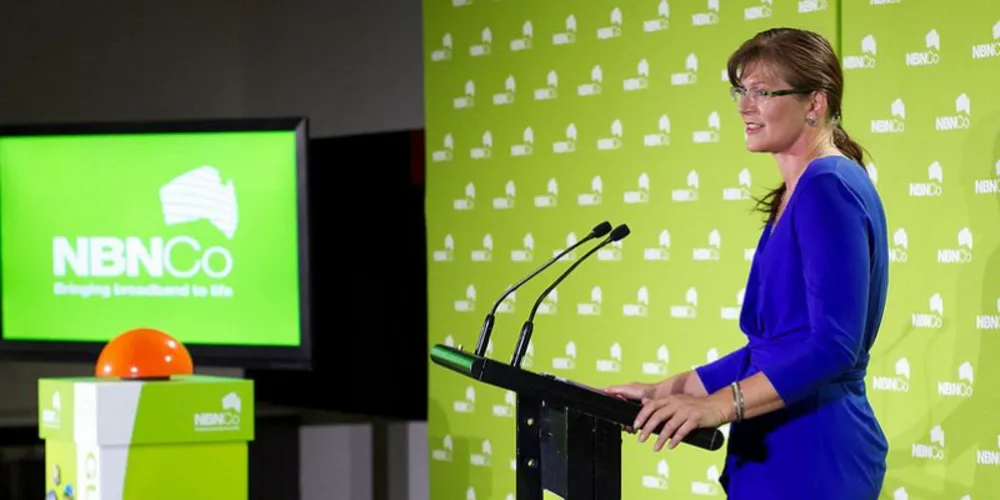 Presenter at the NBN Co lectern in front of a green branded backdrop and screen